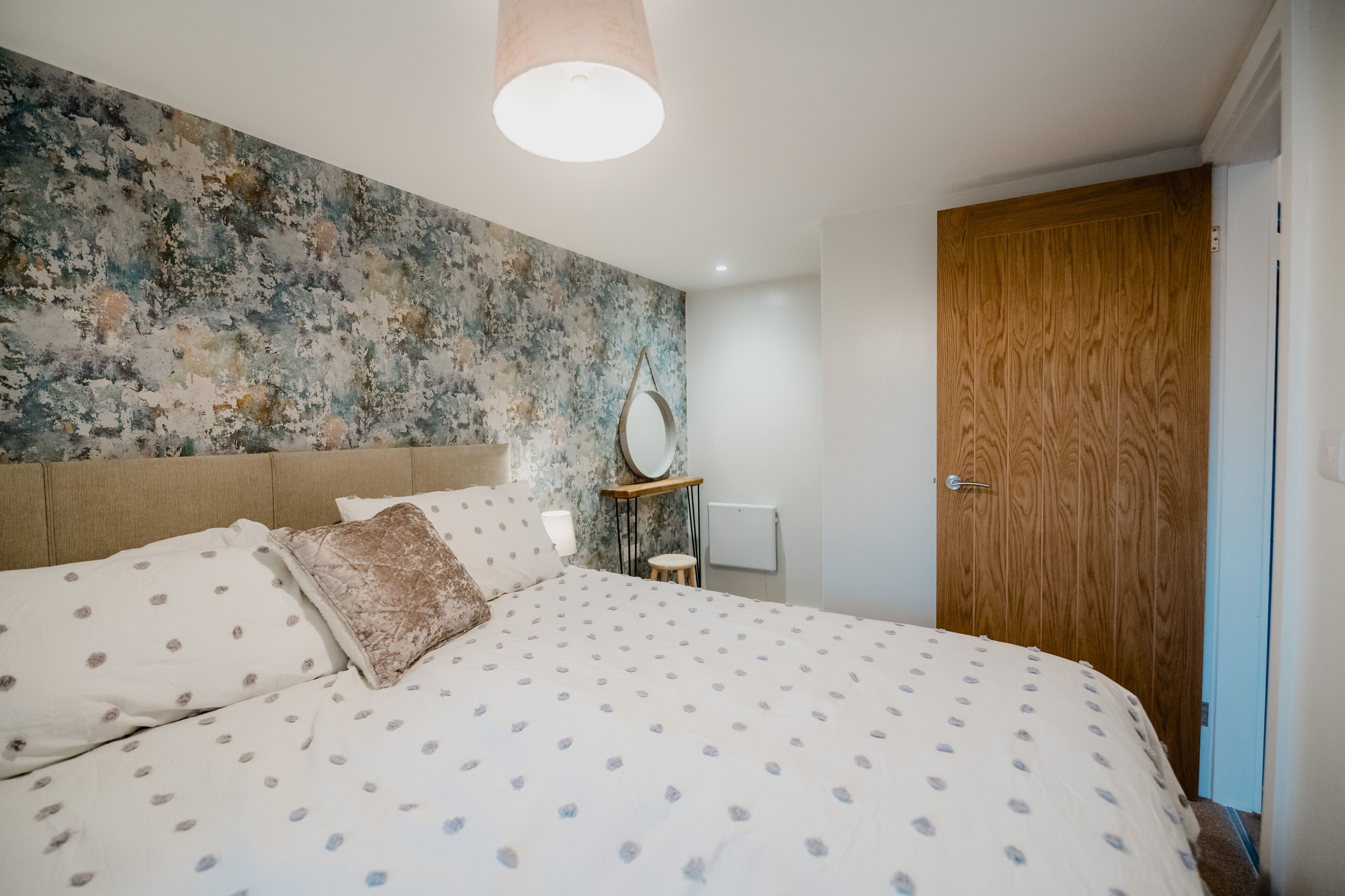 Quarto com cama grande, porta de madeira e parede com textura.