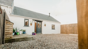 A white house with a grey tiled roof, a wooden fence, and gravel ground. - The Cow Shed at Pencraig (Holyhead)