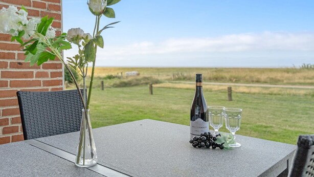 Un tavolo con una bottiglia di vino Silverbloom, due bicchieri e un grappolo d'uva su una terrazza affacciata su un prato e un muro in mattoni.