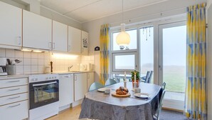 Una cucina moderna con mobili bianchi, un tavolo da pranzo con tovaglia grigia e vista all'esterno attraverso ampie finestre.