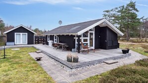 Ein modernes, schwarzes Gebäude mit einer Holzterrasse, einer Satellitenschüssel und einem kleinen Sitzbereich im Freien mit Stühlen und Tischen.
