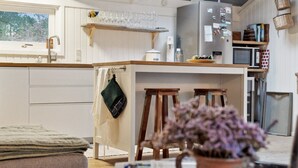 Eine moderne Küche mit weißen Schränken, einem eingebauten Backofen und einem Edelstahl-Kühlschrank. Holzschemeln und eine hängende Küchenutensilienstange sind ebenfalls vorhanden.