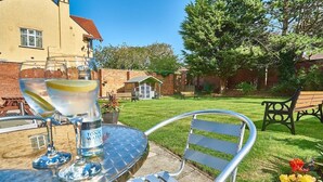 A metal table with two glasses of tonic water and a bottle, a metal chair, and a bench in a backyard with a house in the background. - The Salfordian Hotel (Southport)
