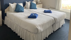 A double bed with white and blue bedding, a bedside table with a lamp, and a window with curtains. - The Salfordian Hotel (Southport)