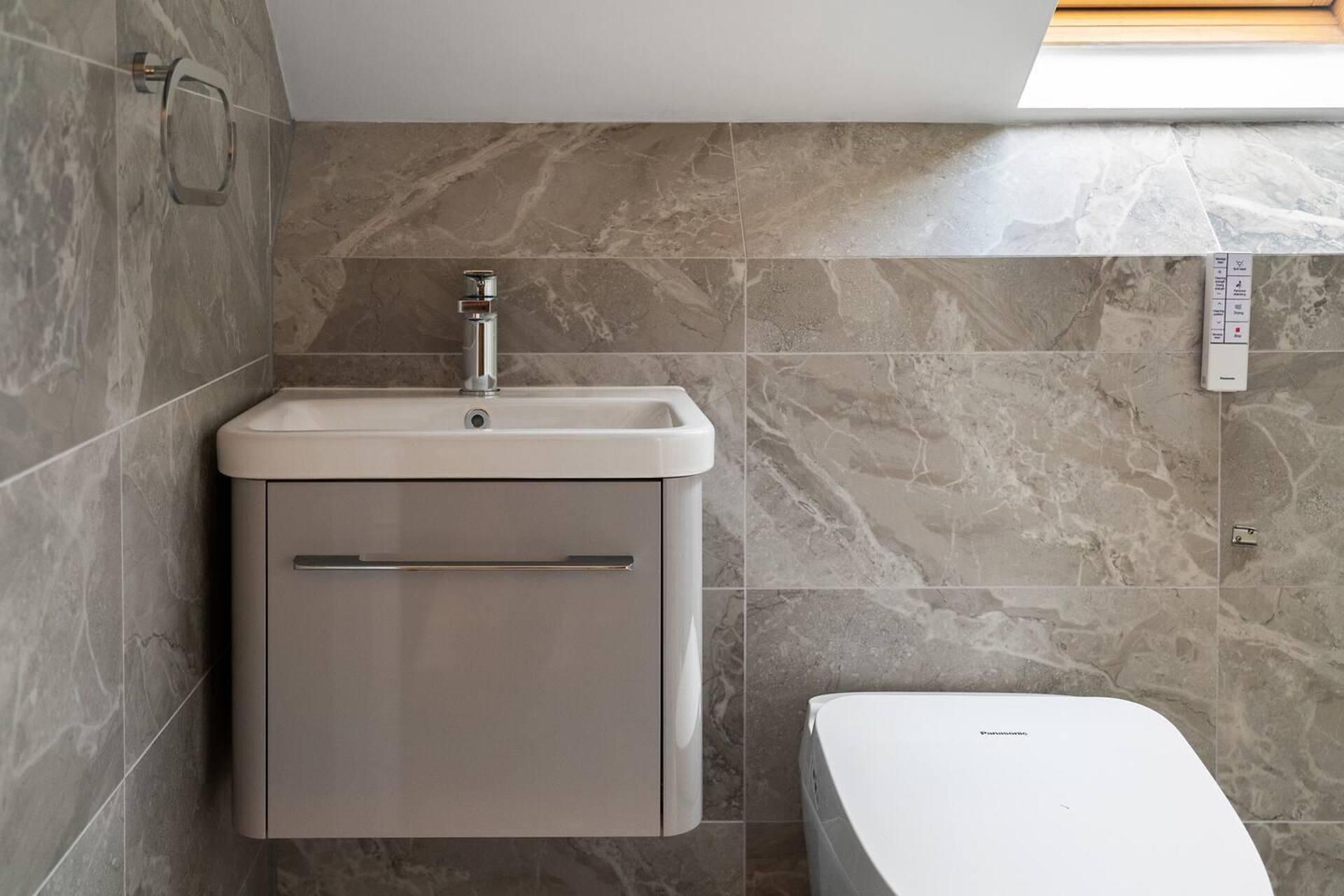 A bathroom with a built-in sink, a toilet, and a wall-mounted control panel.