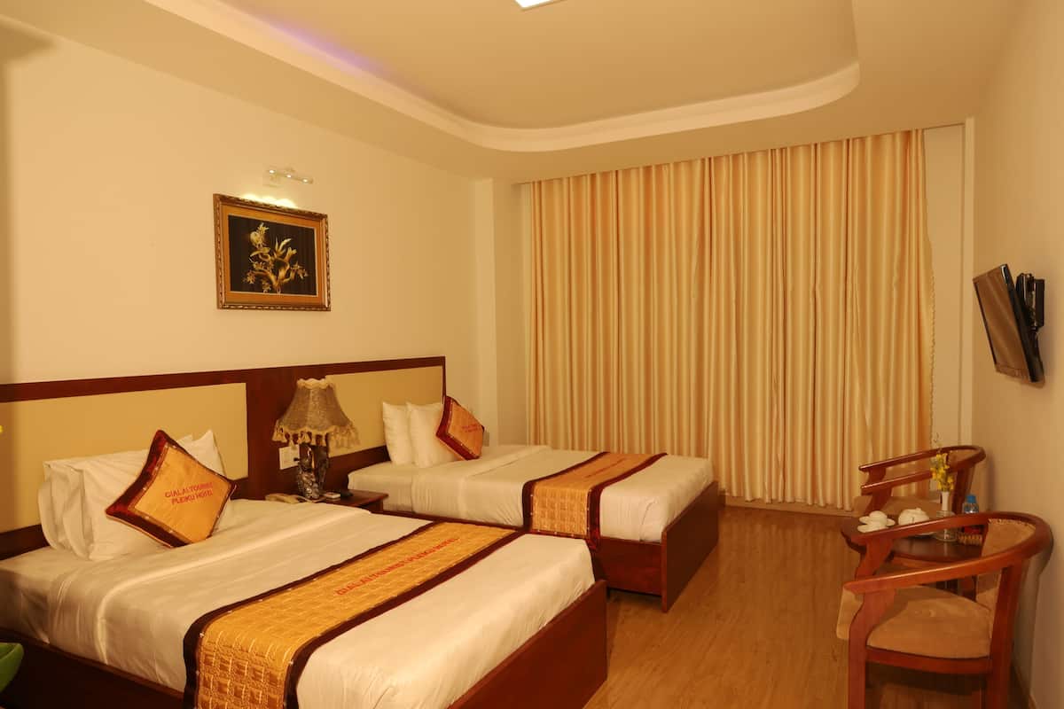A hotel room with two beds, a wooden chair, a table, a lamp, a framed picture, and a curtain.