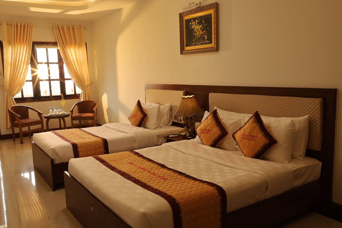 A hotel room with two beds, a small table, chairs, and a window with curtains.