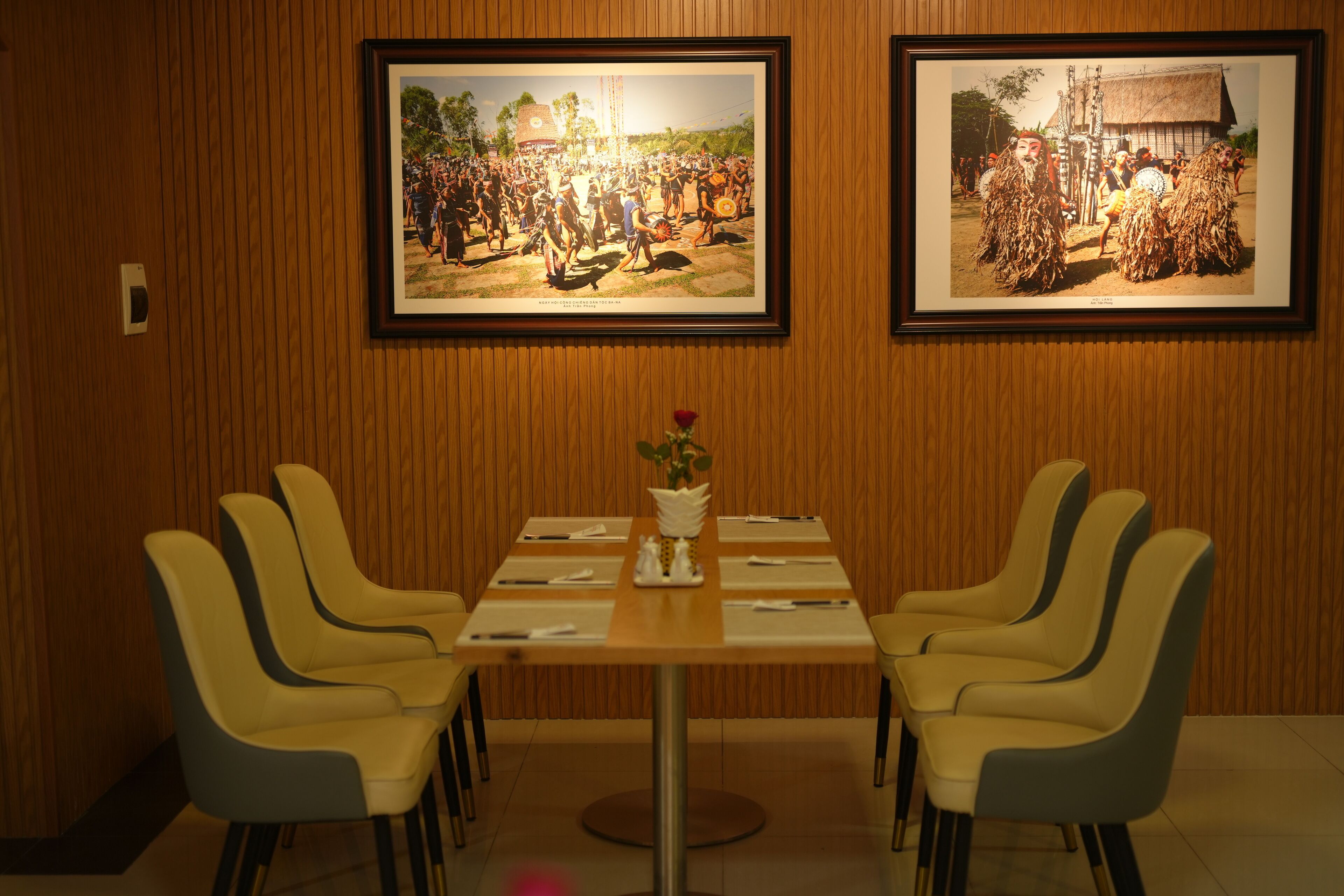Un comedor con pared de madera, cuadros enmarcados, una mesa con un jarrón de flores y cuatro sillas.