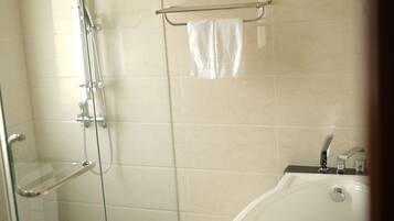 A bathroom with a glass shower enclosure, a towel rack with a towel, and a bathtub with a faucet.
