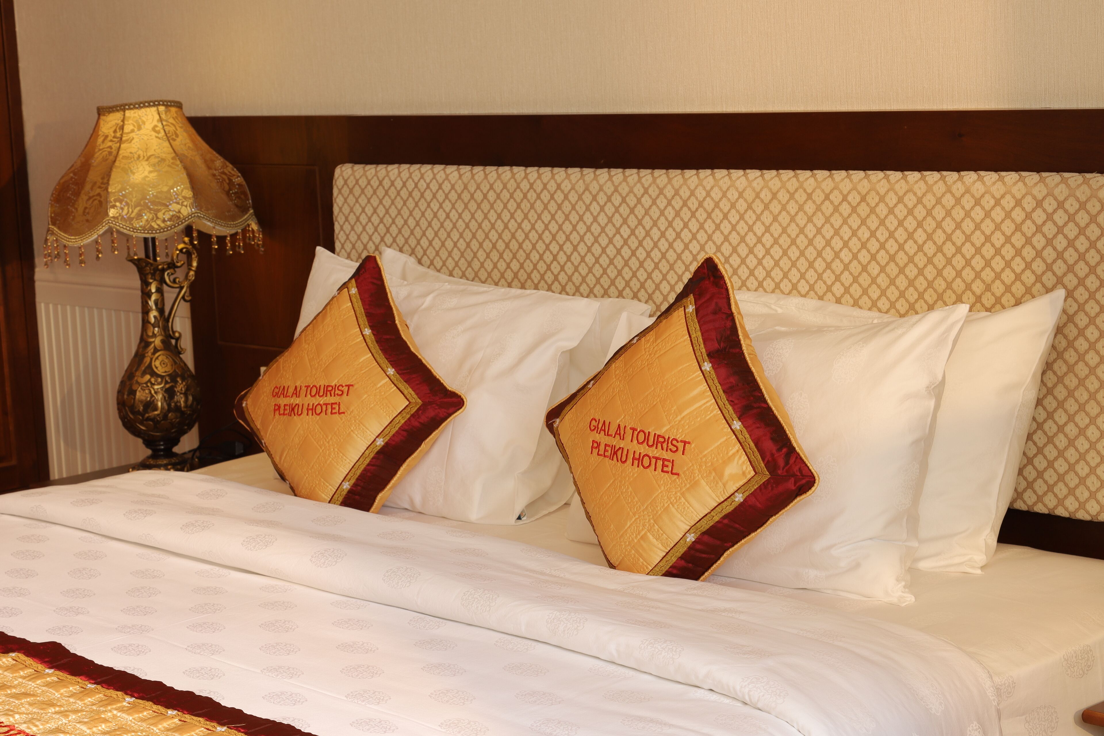 Cama bem arrumada com lençóis brancos e duas almofadas decorativas com detalhes dourados e texto.