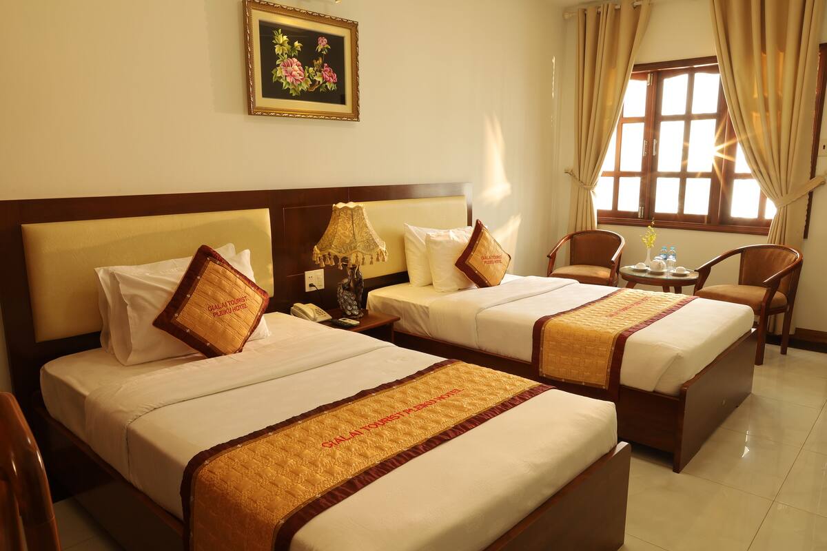 A hotel room with two beds, a nightstand, a table with chairs, and a window with curtains.