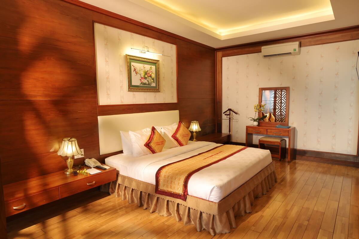 A hotel room with a large bed, bedside tables, a desk, and a mirror.