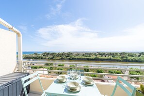 A balcony with a table set for dining, overlooking a river and greenery. - 0116-MUGA PARK Apartment with river and sea view (Empuriabrava)