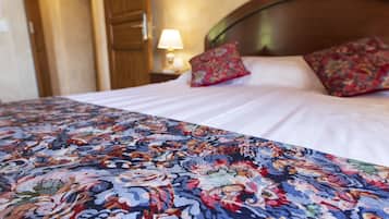 Un lit avec une couvre-lit à motifs floraux, une tête de lit en bois et deux oreillers rouges.