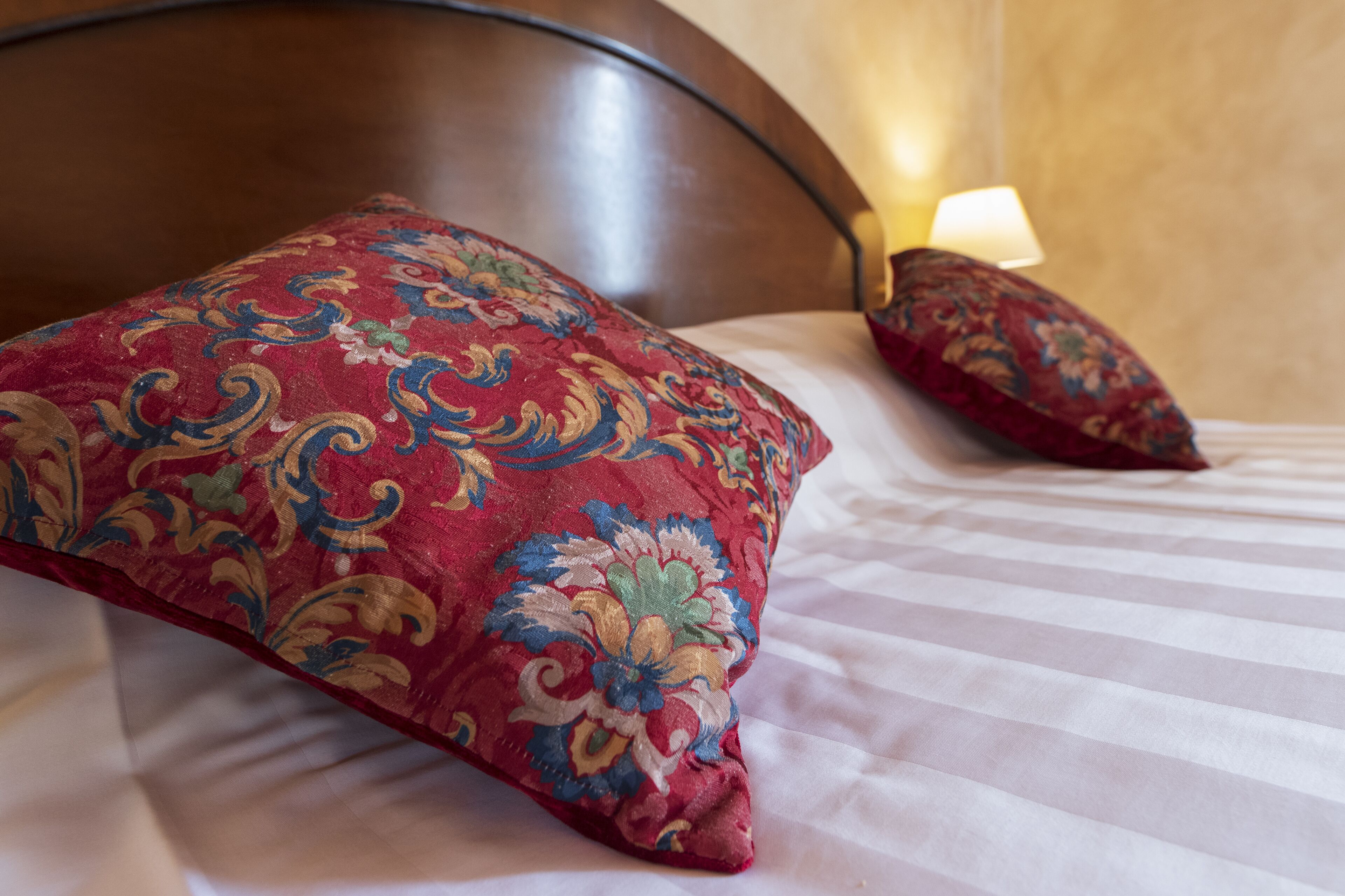 Una cama con cabecera de madera, ropa de cama a rayas y dos almohadas decorativas.