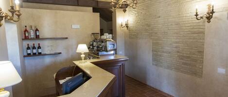 A bar area with a wooden counter, shelves with bottles, a coffee machine, and a brick floor.