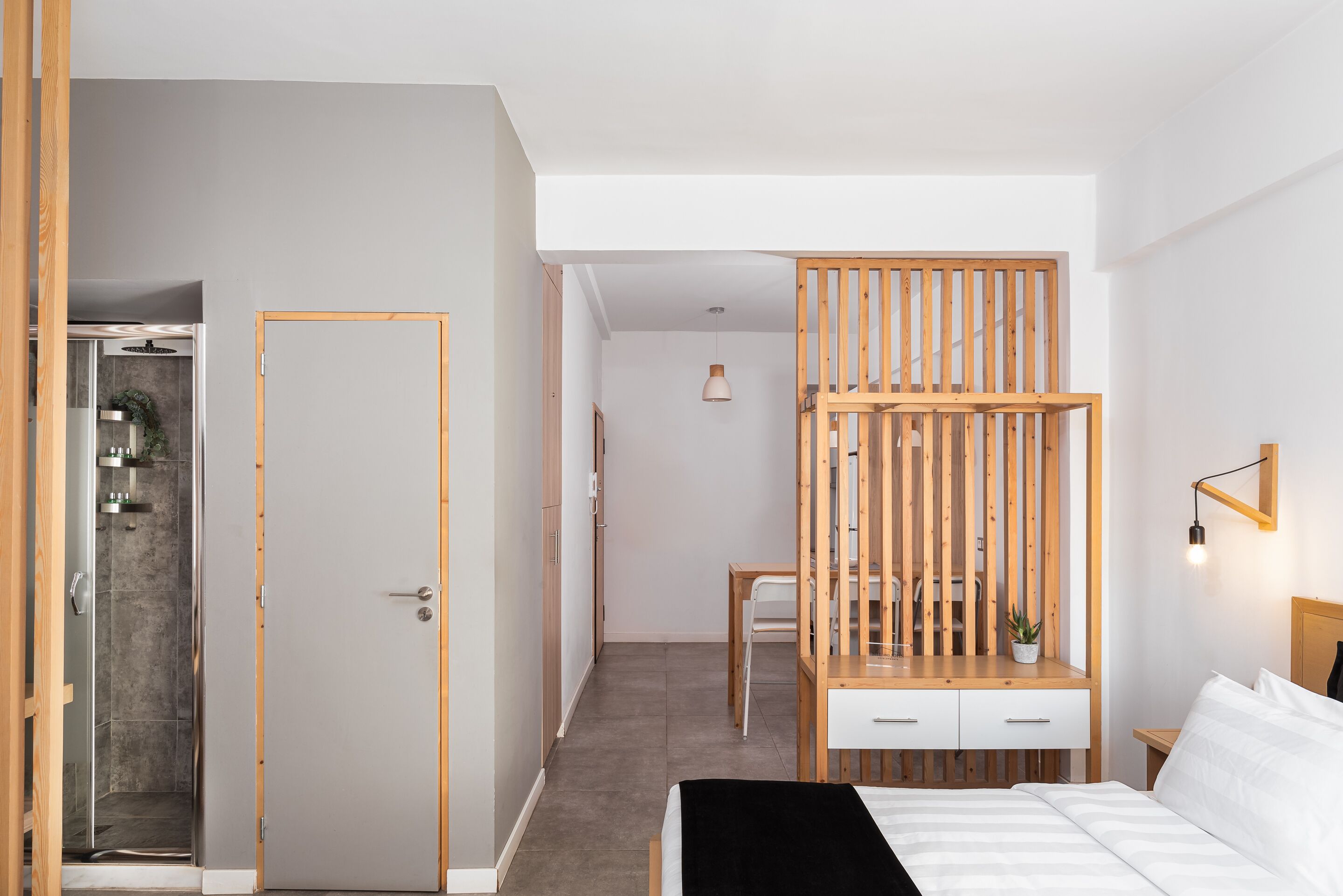 A modern bedroom with a bed, a wooden desk, a chair, and a small table with a plant.