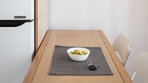 A modern kitchen with a white refrigerator, a wooden table with a bowl of fruit, and a pendant light. - Acropolis Cozy Living (Athens)