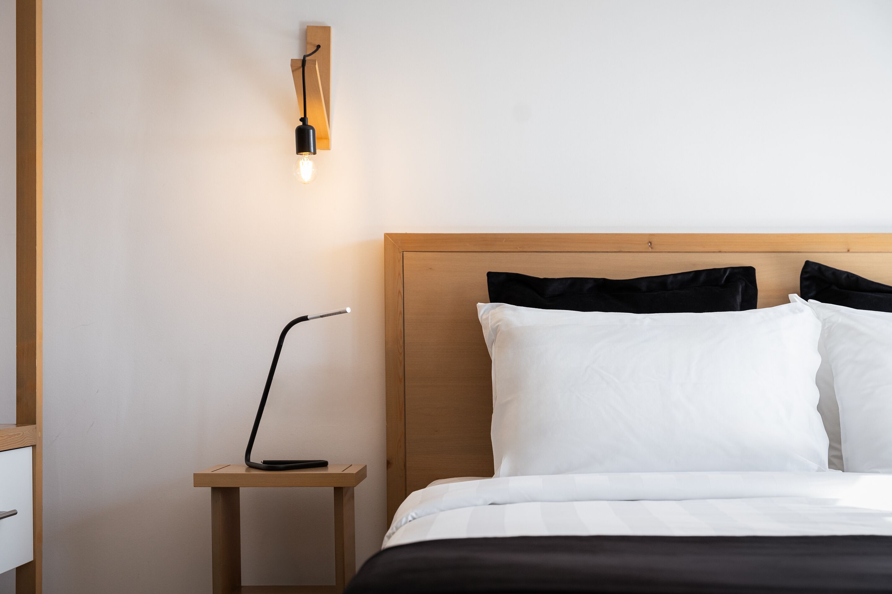 A neatly made bed with white and black bedding, a wooden headboard, and a bedside table with a lamp.