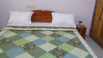 A bed with a quilt, pillows, a wooden headboard, a nightstand with a small plant, and a door.