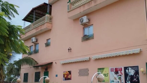 Un edificio rosa con varios balcones, unidades de aire acondicionado y un pequeño jardín con palmeras.