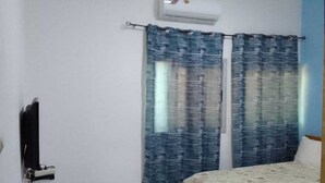 Un dormitorio con cama, cortina, unidad de aire acondicionado y televisor montado en la pared.