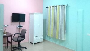 Una habitación con una pared rosa, un armario blanco, un escritorio con una silla y un televisor.
