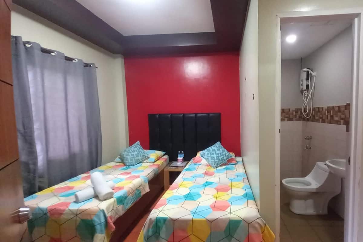 A room with two beds, a red wall, a shower area, and a toilet.