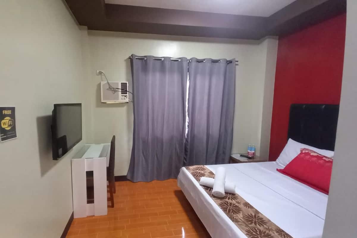 A hotel room with a bed, a desk, a television, and a window with curtains.