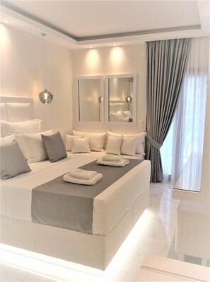 Une chambre d’hôtel moderne avec un grand lit, des tables de chevet, un miroir et une vue sur l’extérieur.