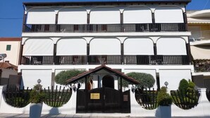 Ein zweistöckiges Gebäude mit einer symmetrischen Fassade, einem zentralen Eingang mit einem schwarzen Tor und zwei Balkonen im oberen Geschoss.