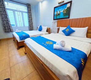 A hotel room with two beds, each with a blue bedspread and a towel. There is a painting on the wall and a window with curtains.