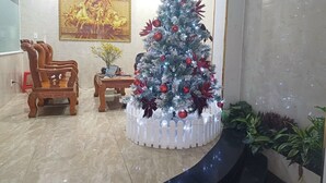 A lobby with a Christmas tree, wooden chairs, a small table with a vase, and a painting on the wall. - Cozy Hotel HCM (Ho Chi Minh City)