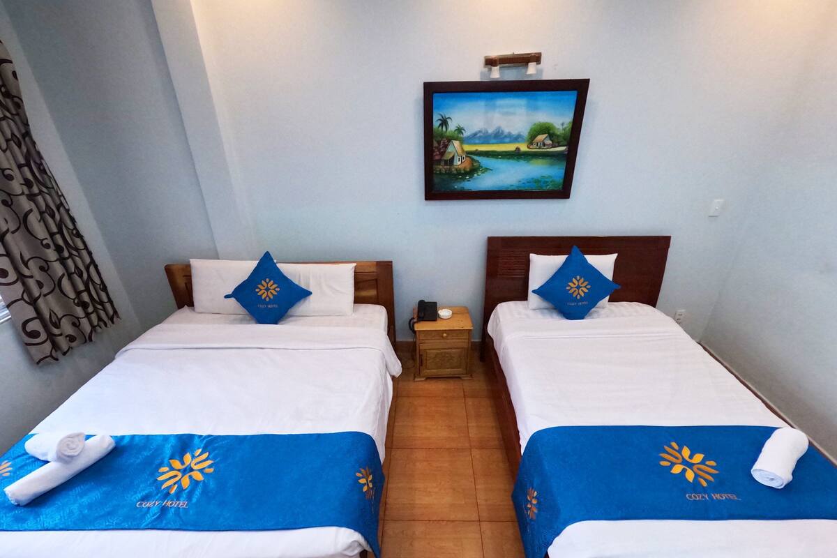 Dos camas individuales con colchas y almohadas azules a juego, cada una con un logotipo, en una habitación con suelo de madera y un cuadro en la pared.