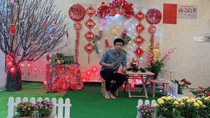 A man sitting on a stool in a decorated indoor space with a table, red lanterns, and floral arrangements. - Cozy Hotel HCM (Ho Chi Minh City)