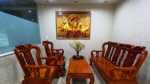 A room with a wooden sofa and chairs, a small table with a vase of flowers, and a framed picture on the wall. - Cozy Hotel HCM (Ho Chi Minh City)