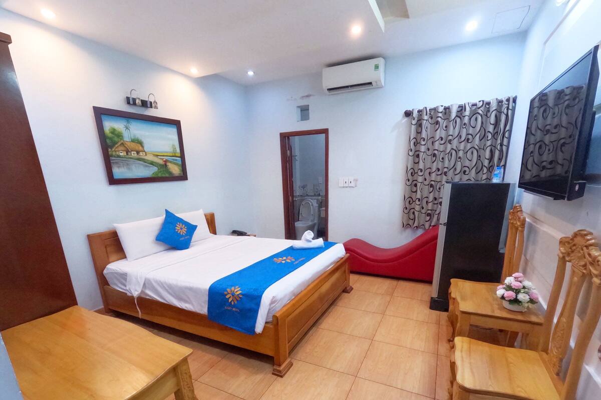 Una habitación de hotel con cama, escritorio, silla, televisión y aire acondicionado.