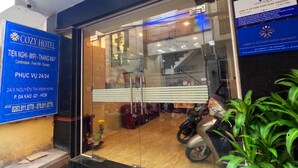 A hotel entrance with a signboard indicating amenities like WiFi, elevator, and 24/7 service. - Cozy Hotel HCM (Ho Chi Minh City)