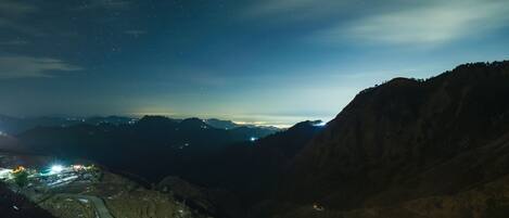 A night view of a mountainous landscape with a valley and distant city lights.