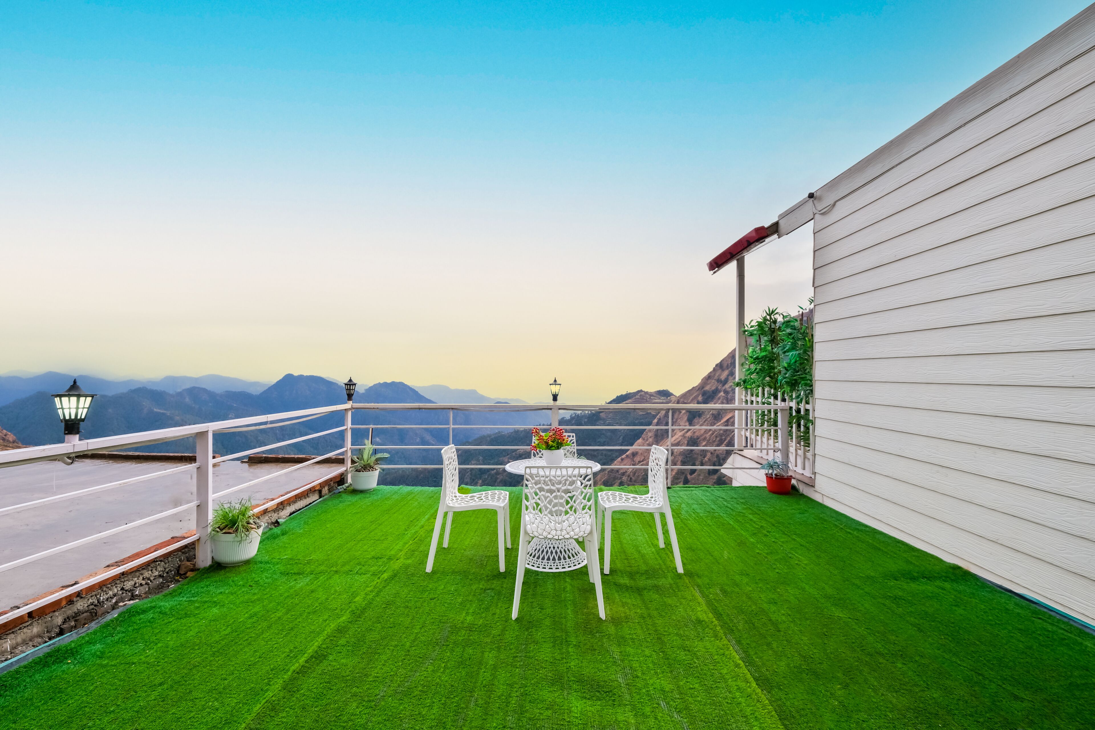 A balcony with a white railing, a small round table with chairs, and potted plants.
