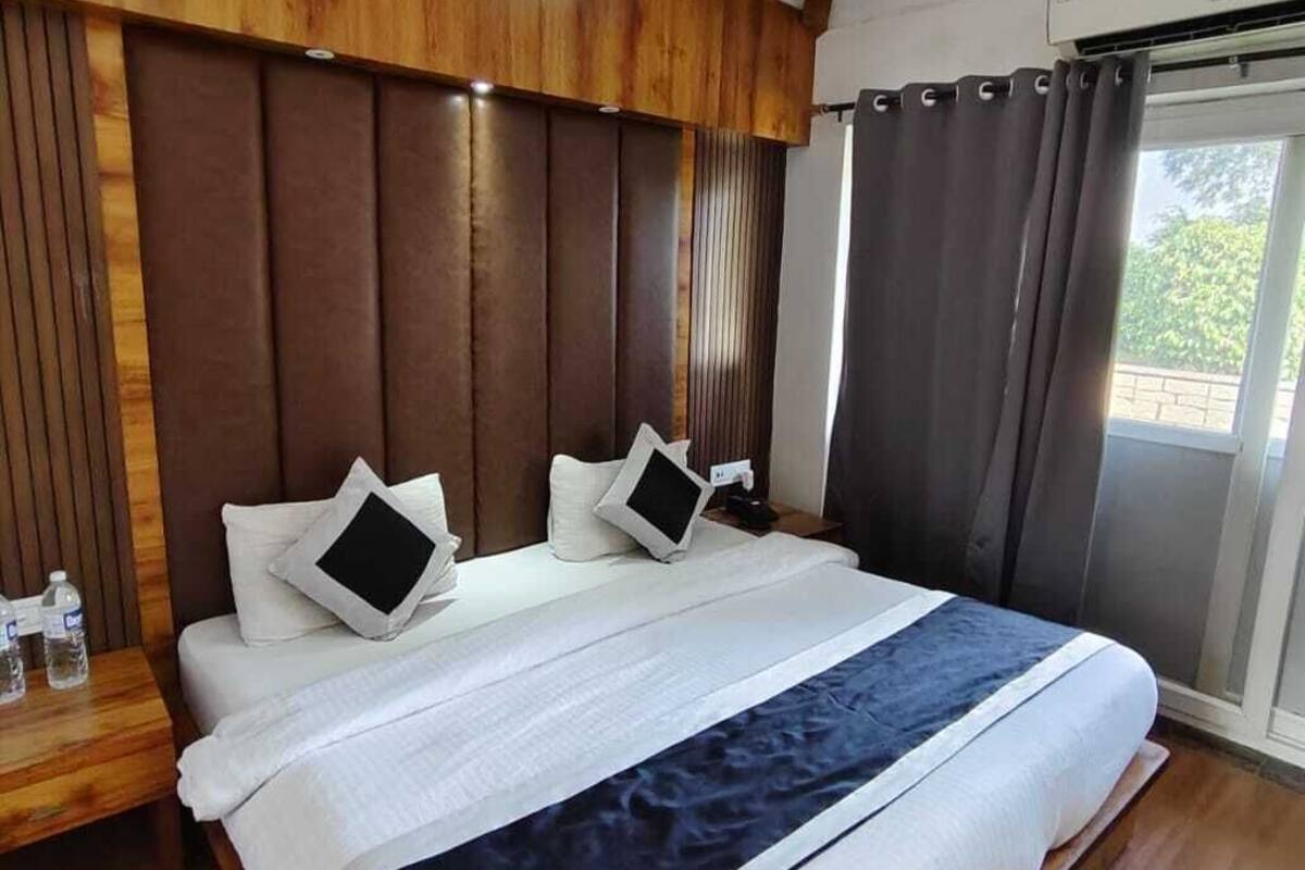 A modern bedroom with a large bed, wooden headboard, and a view of greenery outside.