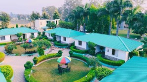 A resort with multiple bungalow-style buildings, a central lawn with a colorful umbrella, and well-manicured gardens. - Royals Moonlight Resort (Kaladhungi)