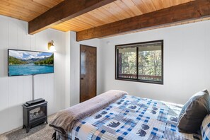 A bedroom with a bed, a television, a window, and a fireplace.
