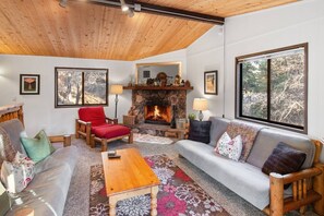 A cozy living room with a fireplace, wooden furniture, and large windows.
