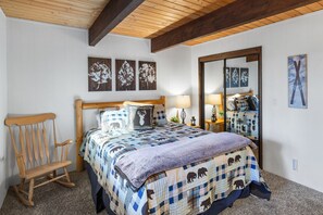A bedroom with a wooden bed frame, a rocking chair, a quilted bedspread, and a large mirror. - Sunset Mountain Retreat By Destination Big Bear: Nestled in Lower Moonridge! 1 Mile Away from Bear Mountain Ski Resort, Golf Course and Zoo! Reverse Floor Plan!  Air Hockey Game Table! (Big Bear Lake)