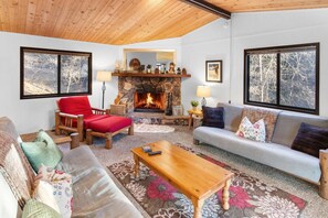 A cozy living room with a fireplace, wooden furniture, and large windows. - Sunset Mountain Retreat By Destination Big Bear: Nestled in Lower Moonridge! 1 Mile Away from Bear Mountain Ski Resort, Golf Course and Zoo! Reverse Floor Plan!  Air Hockey Game Table! (Big Bear Lake)