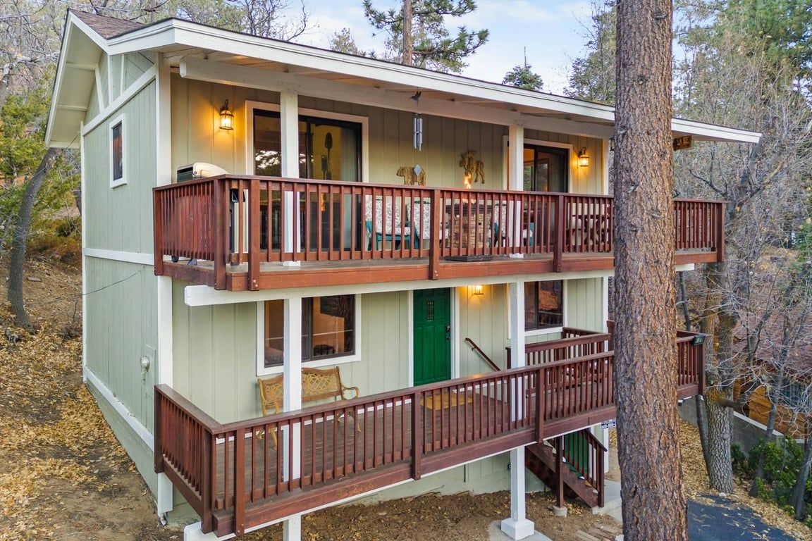 Une cabane à deux étages avec un balcon à l’étage supérieur, une porte verte et un escalier apparent.