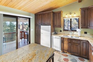 A kitchen with wooden cabinets, a granite countertop, a refrigerator, and a dishwasher. - Sunset Mountain Retreat By Destination Big Bear: Nestled in Lower Moonridge! 1 Mile Away from Bear Mountain Ski Resort, Golf Course and Zoo! Reverse Floor Plan!  Air Hockey Game Table! (Big Bear Lake)