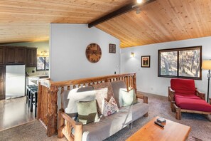 A cozy living area with a wooden ceiling, a sofa with cushions, a red chair, and a view of the outdoors through a window. - Sunset Mountain Retreat By Destination Big Bear: Nestled in Lower Moonridge! 1 Mile Away from Bear Mountain Ski Resort, Golf Course and Zoo! Reverse Floor Plan!  Air Hockey Game Table! (Big Bear Lake)