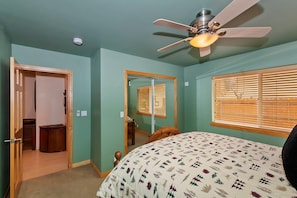 A bedroom with a bed, a ceiling fan, a window with blinds, and a door leading to another room.